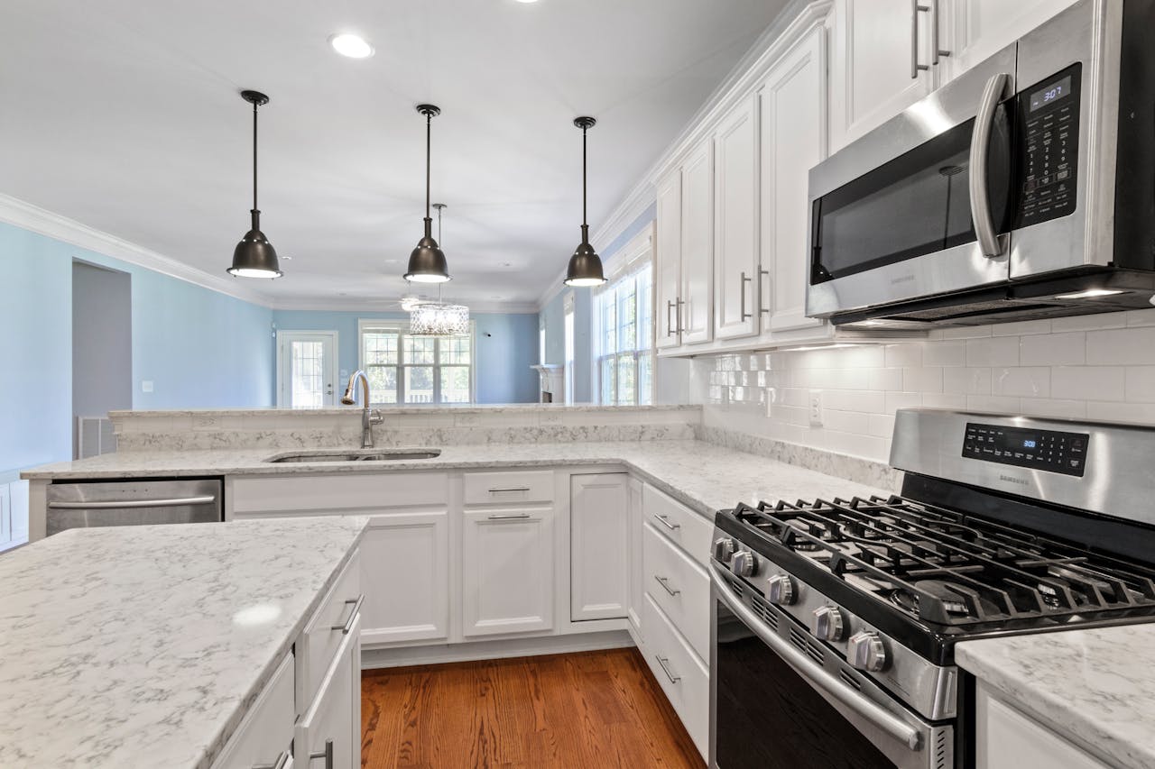 Sleek kitchen featuring stainless steel appliances and marble countertops under pendant lighting.