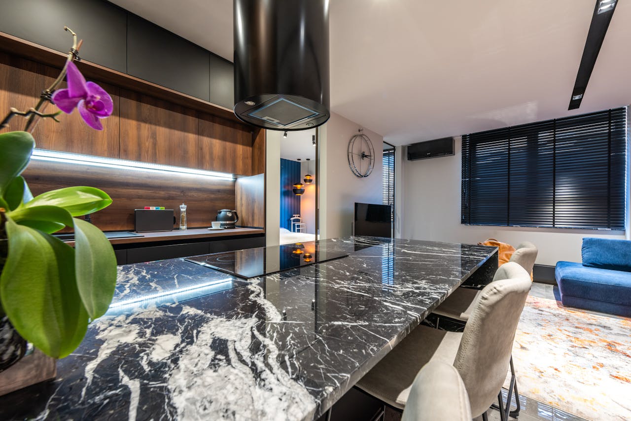 Contemporary kitchen with moth orchid on marble table with hob under hood against living room at home